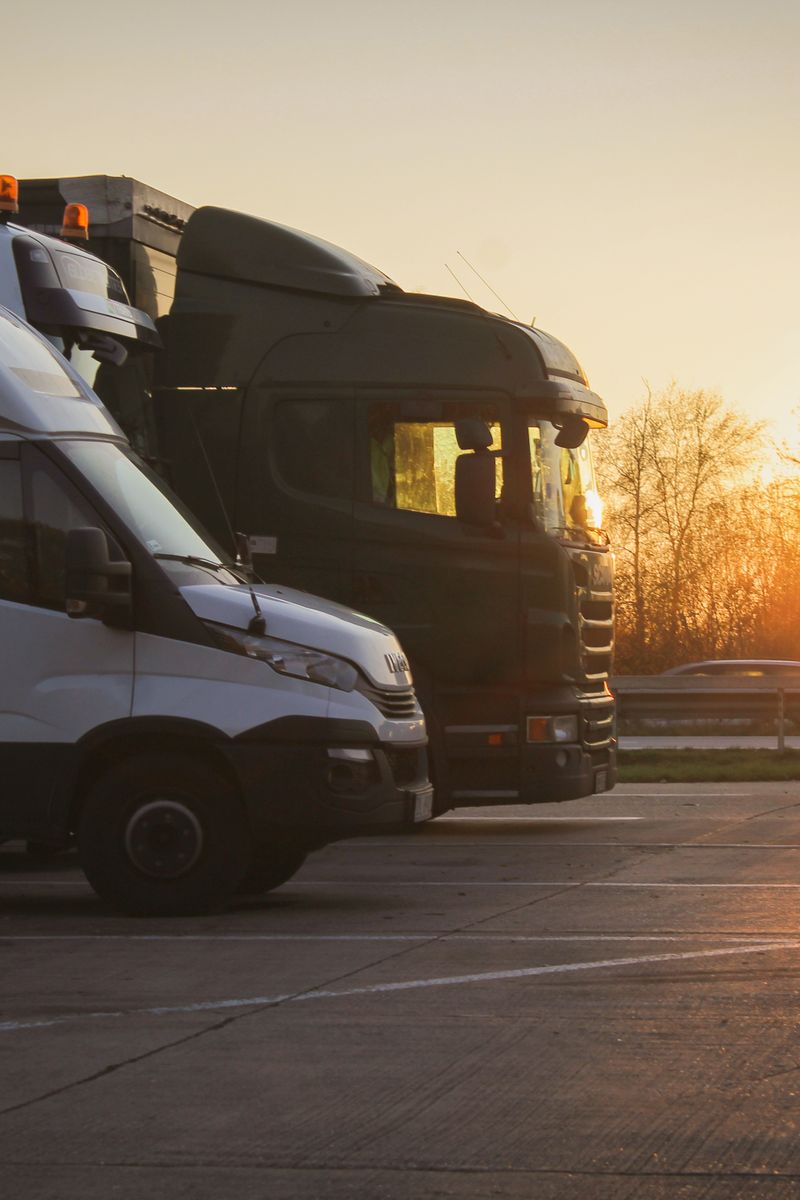 A row of trucks and car transporter parked at sunset in an open parking lot, highlighting the golden hour.